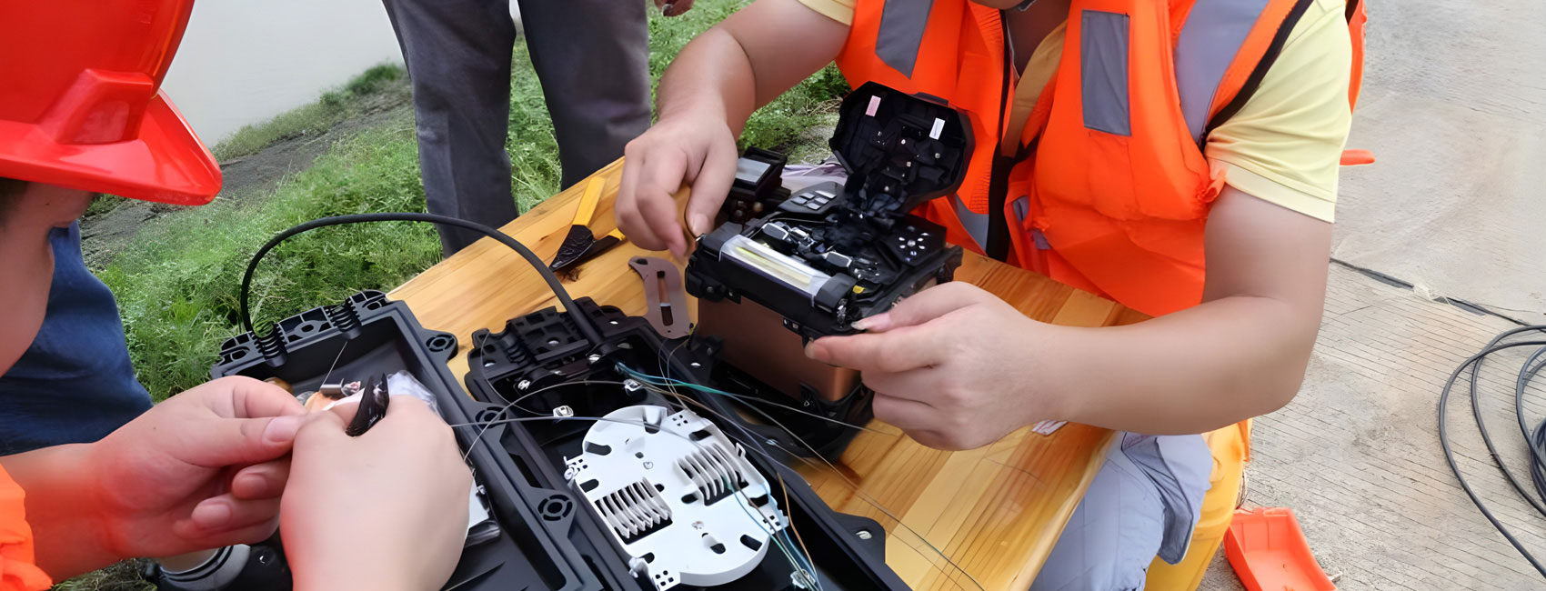 Engineer using a fiber fusion splicer outdoors, connecting cables at a field installation site.